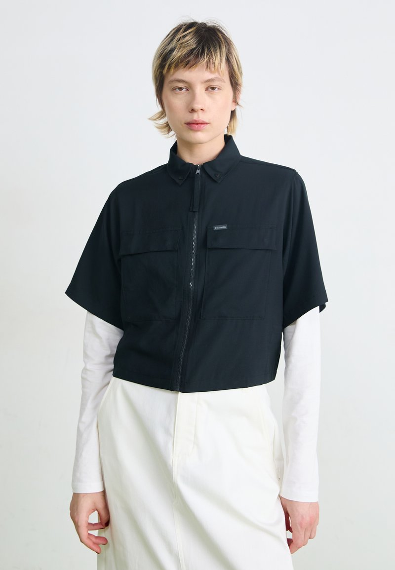 Veste noire à manches courtes et fermeture éclair, avec deux poches poitrine. Fabriquée en tissu léger, elle présente un col et une coupe ample.
