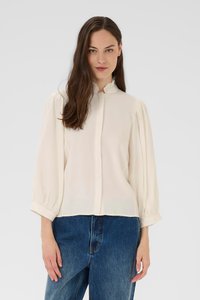 Blouse de couleur crème avec un col fronc�é, des manches bouffantes et un devant à boutons ; fabriquée en tissu léger et doux avec une coupe décontractée.
