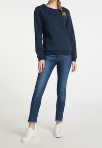 Sudadera azul marino con cuello redondo y puños acanalados, combinada con jeans azules ajustados y zapatillas blancas. Tejido suave con un corte relajado.
