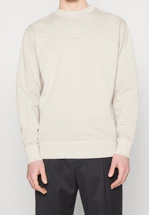 Ljust beige sweatshirt med rund halsringning, diskret logotyp på bröstet, ribbade ärmslut och fåll, samt en avslappnad passform. Passar för vardagsbruk.