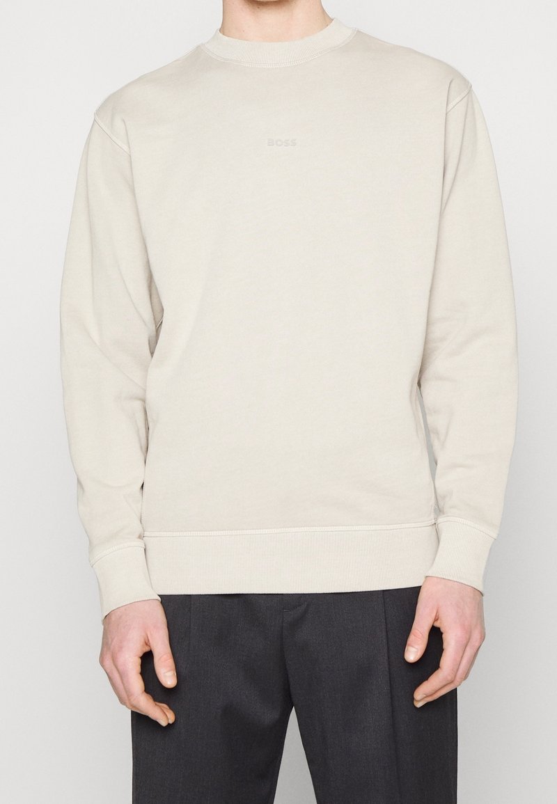 Felpa beige chiaro con collo tondo, logo discreto sul petto, polsini e orlo a coste, e una vestibilità rilassata. Adatta per un abbigliamento casual.