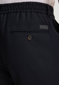 Granatowe dresy z elastycznym pasem, o teksturowanej tkaninie, z tylną kieszenią z guzikiem i małą czarną łatą z logo.