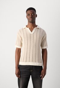 Cremfarbener gestrickter Poloshirt mit V-Ausschnitt, kurzen Ärmeln, strukturiertem Zickzackmuster und geripptem Saum sowie Kragen.