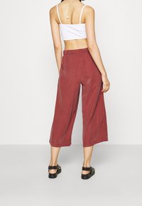 Pantalon culotte bordeaux à coupe décontractée, taille élastique et texture lisse, associé à des sandales noires. Vue arrière affichée.