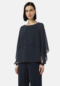 Marineblaue, schichtweise Bluse aus leichtem, durchsichtigen Stoff mit rundem Ausschnitt und weiten Ärmeln, kombiniert mit dunklen Hosen.