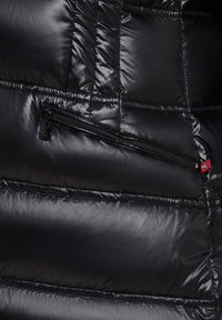 Zwarte donsjacket met een glanzende, gequiltte afwerking, horizontale stiksels en een ritszak met contrasterende hardwaredetails.