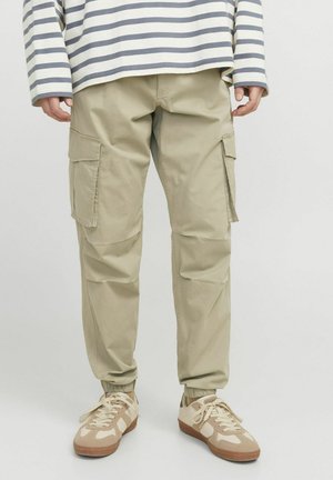 Beige cargobroek met elastische boorden, zijzakken en een relaxte pasvorm. Gecombineerd met bruin- en crèmekleurige sneakers en een gestreepte lange mouwen top.