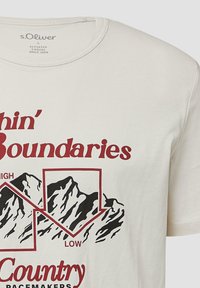 Biała koszulka z czerwonym napisem "Within Boundaries" i czarną grafiką gór przedstawiających wysokie i niskie szczyty, rozmiar L, marka s.Oliver.