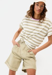 Gestreiftes kurzärmliges T-Shirt in Beige und Weiß mit pinkem Ausschnitt, kombiniert mit hellbeigen Shorts mit seitlichen Taschen und umgeschlagenen Säumen.