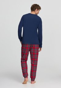 T shirt a maniche lunghe blu navy abbinato a pantaloni del pigiama a quadri rossi con accenti verdi e gialli, realizzati in tessuto morbido, con vita elasticizzata.