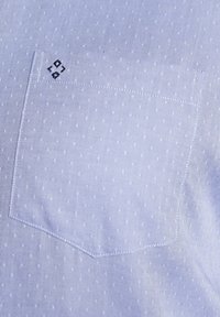 Himmelblaues gemustertes Hemdengewebe mit aufgesetzter Tasche und kleiner gepunkteter Textur. Enthält ein gesticktes Logodetail auf der Tasche.