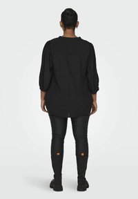 Blusa negra con mangas abullonadas, detalle en el yugo trasero y dobladillo curvo, combinada con pantalones negros ajustados y botas altas hasta la rodilla con acentos naranjas.