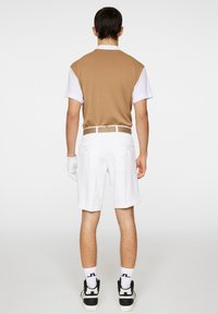 Brązowa i biała koszulka polo z krótkim rękawem z kołnierzykiem, w połączeniu z białymi szortami, uzupełniona białym paskiem i czarnymi butami sportowymi.