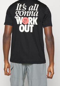 Camiseta negra con texto grande en blanco en la parte posterior: "Todo va a SALIR BIEN" y un emoticono sonriente rojo como acento. Mangas cortas, ajuste estándar.