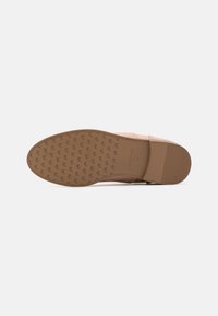 Scarpa beige con suola piatta caratterizzata da un motivo di grip in gomma testurizzata. Materiale superiore liscio con un design a fascia ampia.