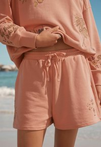 Shorts di cotone color pesco con vita elastica e coulisse, caratterizzati da ricami di un sole e di una bevanda.
