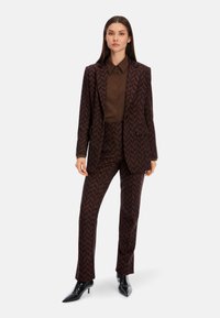 Brown patterned suit with chevron design, featuring a notched lapel blazer and matching trousers, paired with a solid brown button-up shirt.