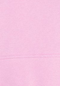 Tessuto rosa chiaro con una texture morbida, con una cucitura ordinata che corre orizzontalmente lungo il fondo. Distribuzione uniforme del colore su tutta la superficie.