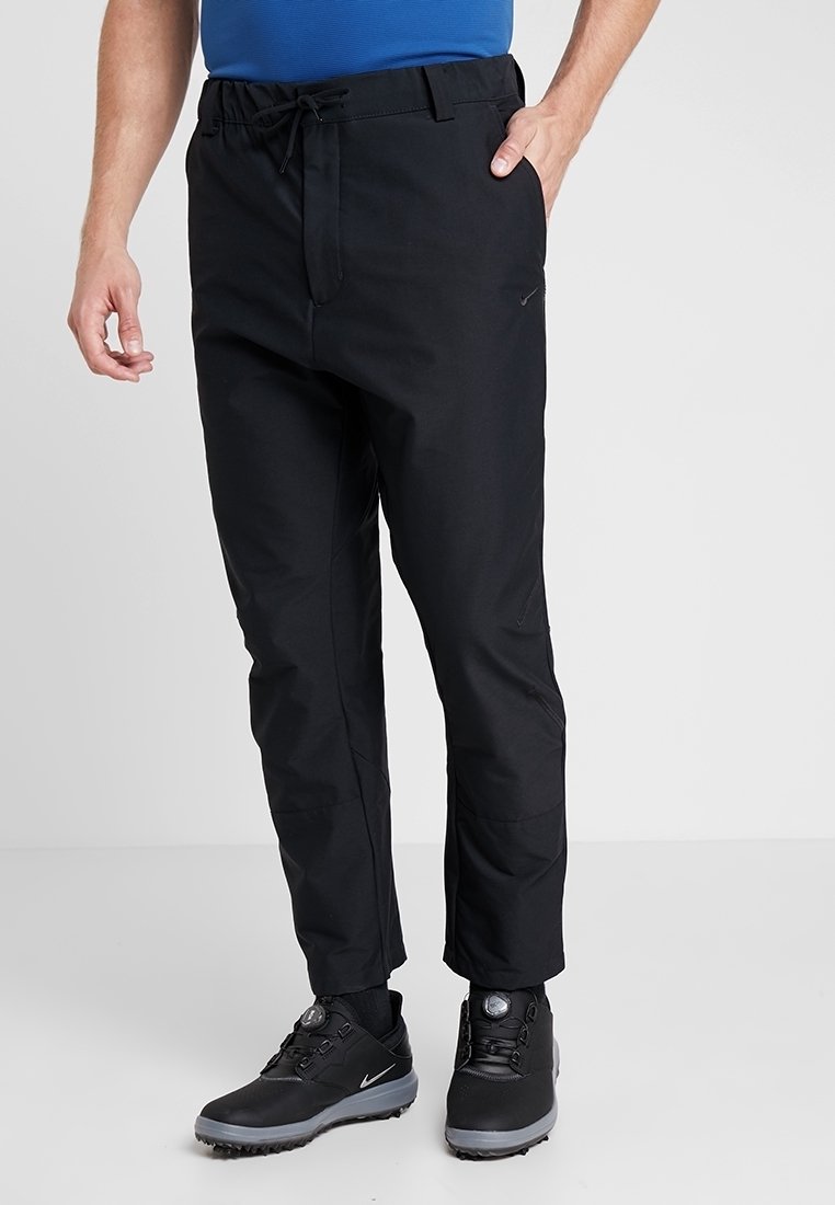 Černé sportovní kalhoty s páskem na stažení v pase, těsně střižené, s reflexním logem, v kombinaci s černými trekovými botami a modrým trikem.