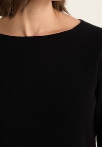 Svart stickad tröja med bred halsringning, långa ärmar och en slät yta. Har förstärkta axelsömmar och en klassisk passform.