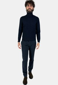Pullover a collo alto in maglia cable-knit di colore navy abbinato a pantaloni scuri e stivali alla caviglia marroni. Design aderente con polsini e orlo a costine.