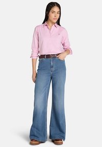 Pink skjorte med knapper kombineret med højtaljede blå vide jeans, brun bælte og chunky brune sko. Glat stof og afslappet pasform.