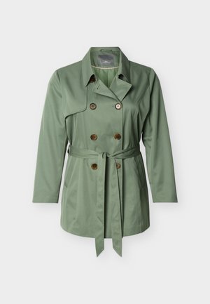 Kahekordse nööbitud salvei-rohelise trench mantliga, millel on suured rinnataskud, pruunid nupud, küljetaskud ja vöökohal seotud kangast vöö.