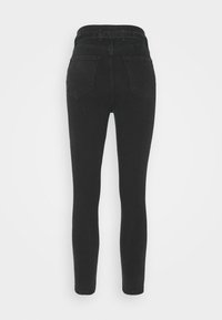 Jean skinny noir taille haute avec passants de ceinture et deux poches arrière, présenté de dos sur un fond uni.