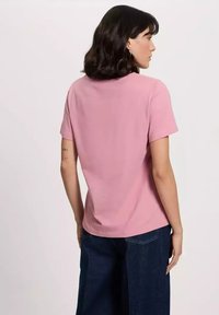 Różowa bawełniana koszulka z krótkim rękawem, okrągłym dekoltem i gładką teksturą. Noszona z ciemnymi dżinsami, pokazana od tyłu.