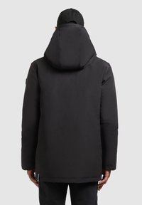 Parka nera isolata con un ampio cappuccio, texture morbida e una vestibilità leggermente ampia. Presenta un sottile marchio sul colletto e sulla cucitura laterale.