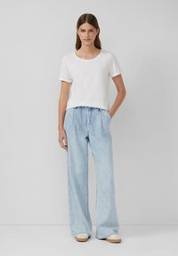Weißes T-Shirt mit kurzen Ärmeln, kombiniert mit hellblauen weit geschnittenen Jeans mit Kordelzugbund, vor einem schlichten Hintergrund präsentiert.