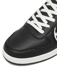 Mustmust musta nahkKing sneaker, valged paelad, perforatsiooniaugud, õmblusdetailid ja valge kummitald valgel taustal.