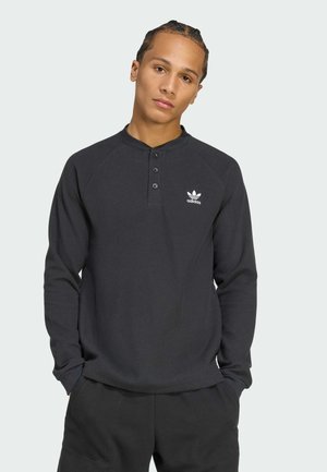 Schwarzes Langarm-Henley-Shirt aus strukturiertem Stoff, mit einer Knopfleiste und einem kleinen weißen Adidas-Logo auf der linken Brust.