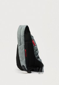 Grå og svart skuldersekk med polstret rygg, røde glidelåstrekkere og justerbar svart rem på hvit bakgrunn.