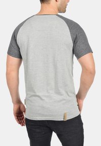 Gray and dark gray short-sleeve t-shirt with a round neckline, featuring a small label at the bottom left and a relaxed fit design.