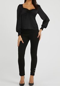 Blusa in raso nero con scollatura quadrata e maniche a sbuffo, abbinata a pantaloni neri aderenti con bottoni argentati sui polsini.