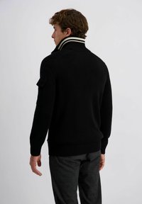 Zwarte trui met hoge kraag en gestreepte accenten. Voorzien van geribde manchetten en zoom, schouderpatchdetails en een gladgebreide textuur.