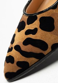 Zapatos planos de estampado de leopardo con una parte superior de ante marrón y detalles en negro, punta afilada y un acabado suave en negro a lo largo de la abertura.