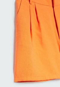 Pantaloni corti arancioni realizzati in tessuto testurizzato con pieghe nella parte frontale e un orlo pulito e rifinito.