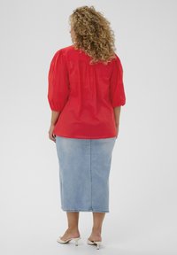Blouse rouge à manches ballons associée à une jupe crayon en denim bleu clair. La tenue présente une texture lisse et une silhouette ajustée.