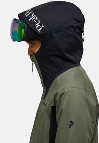 Grüne und schwarze Skijacke mit hohem Kragen, Reißverschluss und Logodetail. Verfügt über eine Kapuze und eine glatte Stofftextur.