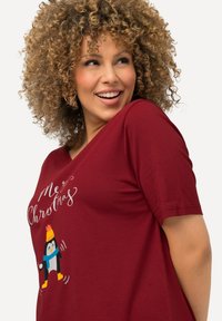Bordeaux kortebragige t-shirt met een afbeelding van een pinguïn in een hoed en sjaal, met de tekst "Me Kerstmis" in witte schreefletters.