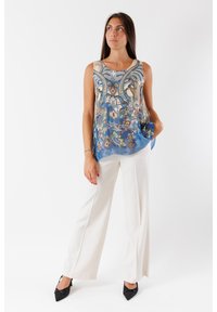 Top floreale blu senza maniche con motivi intricati, abbinato a pantaloni bianchi a gamba larga e tacchi neri a punta. Tessuto morbido, vestibilità rilassata.