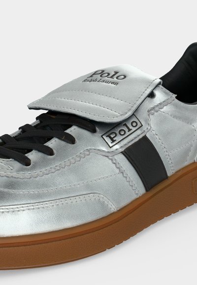 Ασημί δερμάτινο αθλητικό παπούτσι Polo Ralph Lauren με μαύρα κορδόνια, μαύρη πλαϊνή ρίγα και καφέ λαστιχένια σόλα.