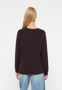 Pullover sweater in dark burgundy knit, featuring a round neckline, long sleeves, and ribbed hem, paired with light blue wide-leg jeans.