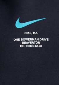 Svart textil med vit och turkos Nike-logotyp och text. Tyget verkar slätt med en fin ribbad struktur.