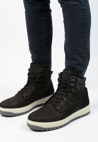 Zwarte hoge laarzen met accent van textuurstof, met opvallende veters, een rubberen zool en een gevoerde kraag voor comfort.