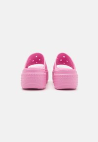 Sabots en caoutchouc rose avec un dos ouvert, dotés de trous de ventilation circulaires et de semelles texturées. Le nom de la marque "crocs" est embossé sur le talon.