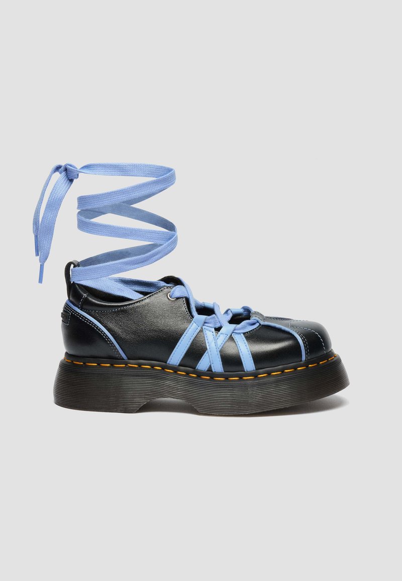 Black platform shoe with thick sole, blue crisscross straps, and long blue ankle wrap laces tied in a bow.