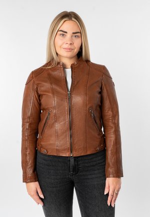 Veste en cuir marron avec un col montant, des coutures verticales et des poches zippées. Finition texturée, coupe ajustée, associée à un pantalon en denim foncé.
